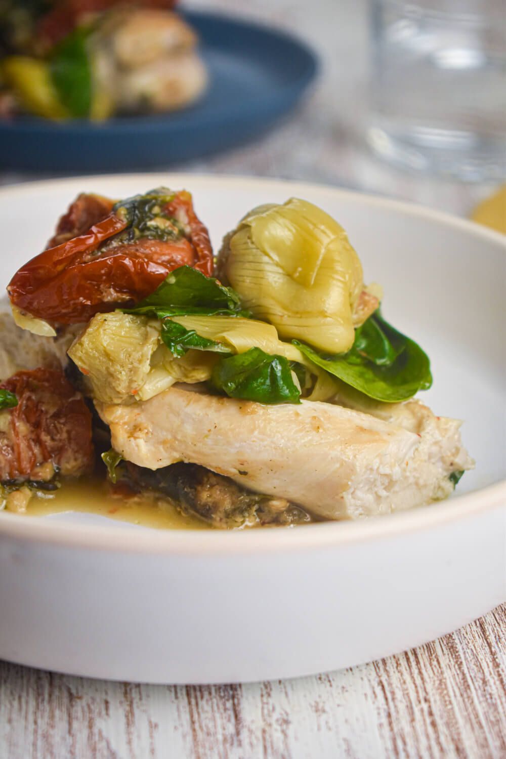 Chicken breasts with spinach and artichoke hearts on a plate with a creamy sauce and sundried tomatoes.