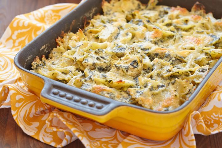 Spinach artichoke pasta with melted cheese in a casserole dish.