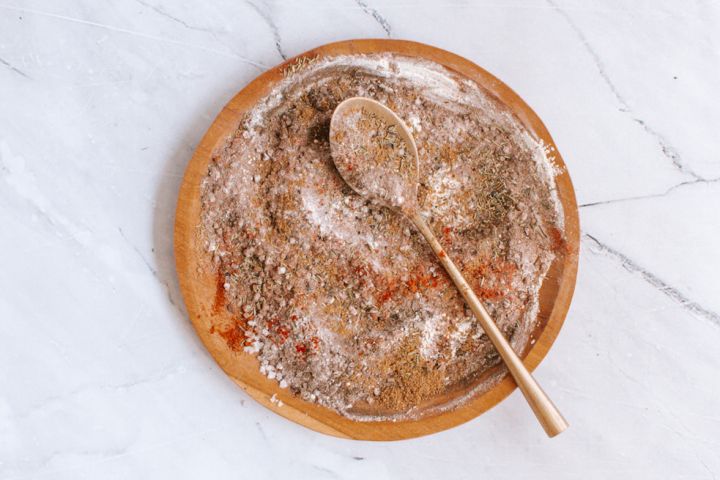 Steak seasoning with kosher salt, pepper, paprika, garlic powder, onion powder, and herbs on a wooden plate.