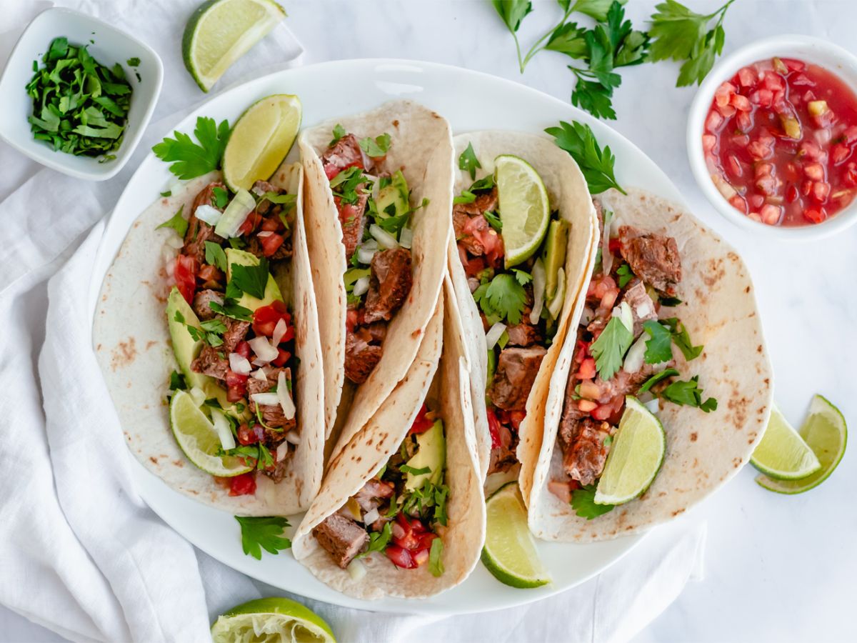 Steak tacos on flour tortillas with cilantro, onion, salsa, and lime.