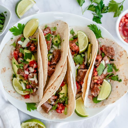 Steak tacos on flour tortillas with cilantro, onion, salsa, and lime.