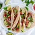 Steak tacos on flour tortillas with cilantro, onion, salsa, and lime.