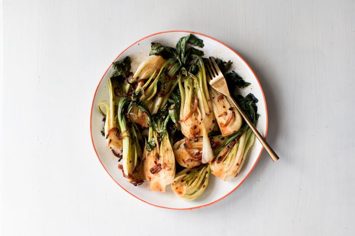 Stir fried bok choy on a plate with red onions, soy sauce, coconut oil, and chili paste.