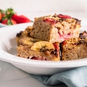 Strawberry baked oatmeal with banana and chocolate chips cut into squares and placed on a white plate.