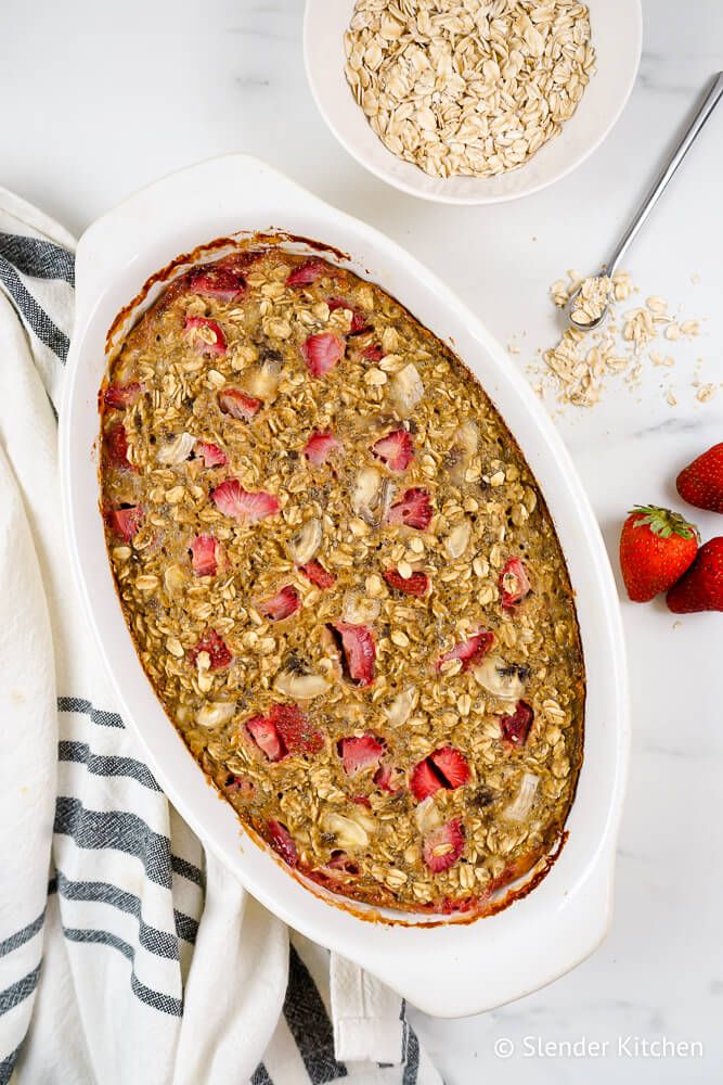 Baked oatmeal with strawberries and bananas in a casserole dish with loose oats and strawberries on the side.