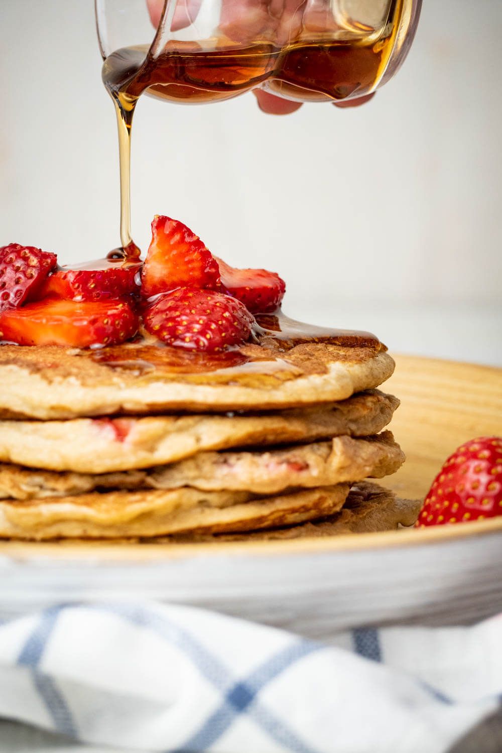 Oatmeal pancakes with fresh strawberries and bananas with maple syrup poured on top.