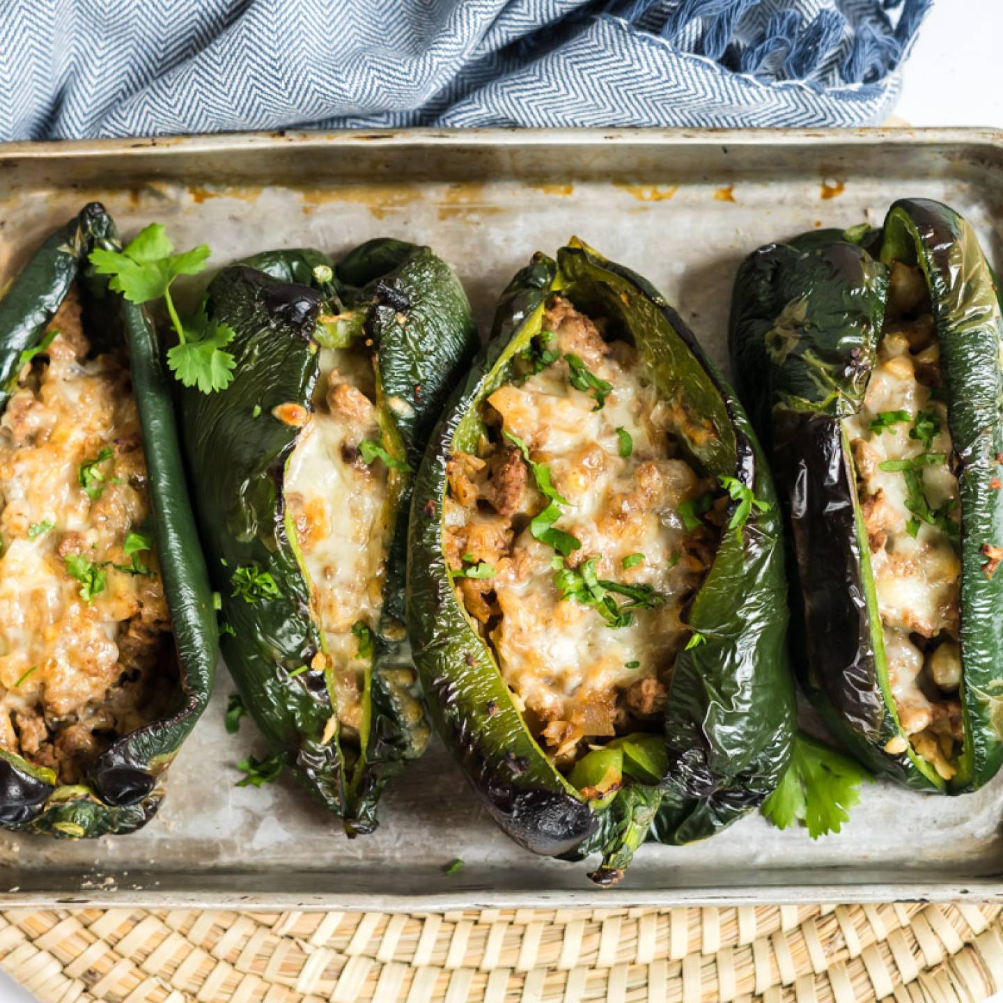 Stuffed poblano peppers with ground turkey, melted cheese, and mozzarella on a baking sheet.