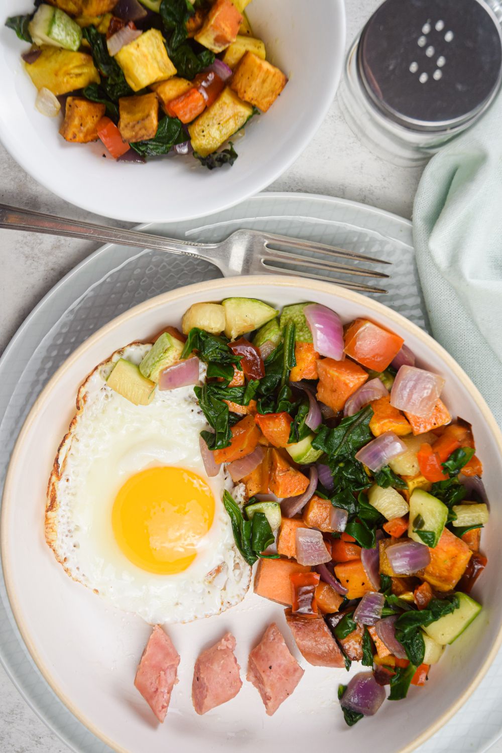 Hash with sweet potatoes, zucchini, peppers, onions, and sausage in a bowl with a fried egg.