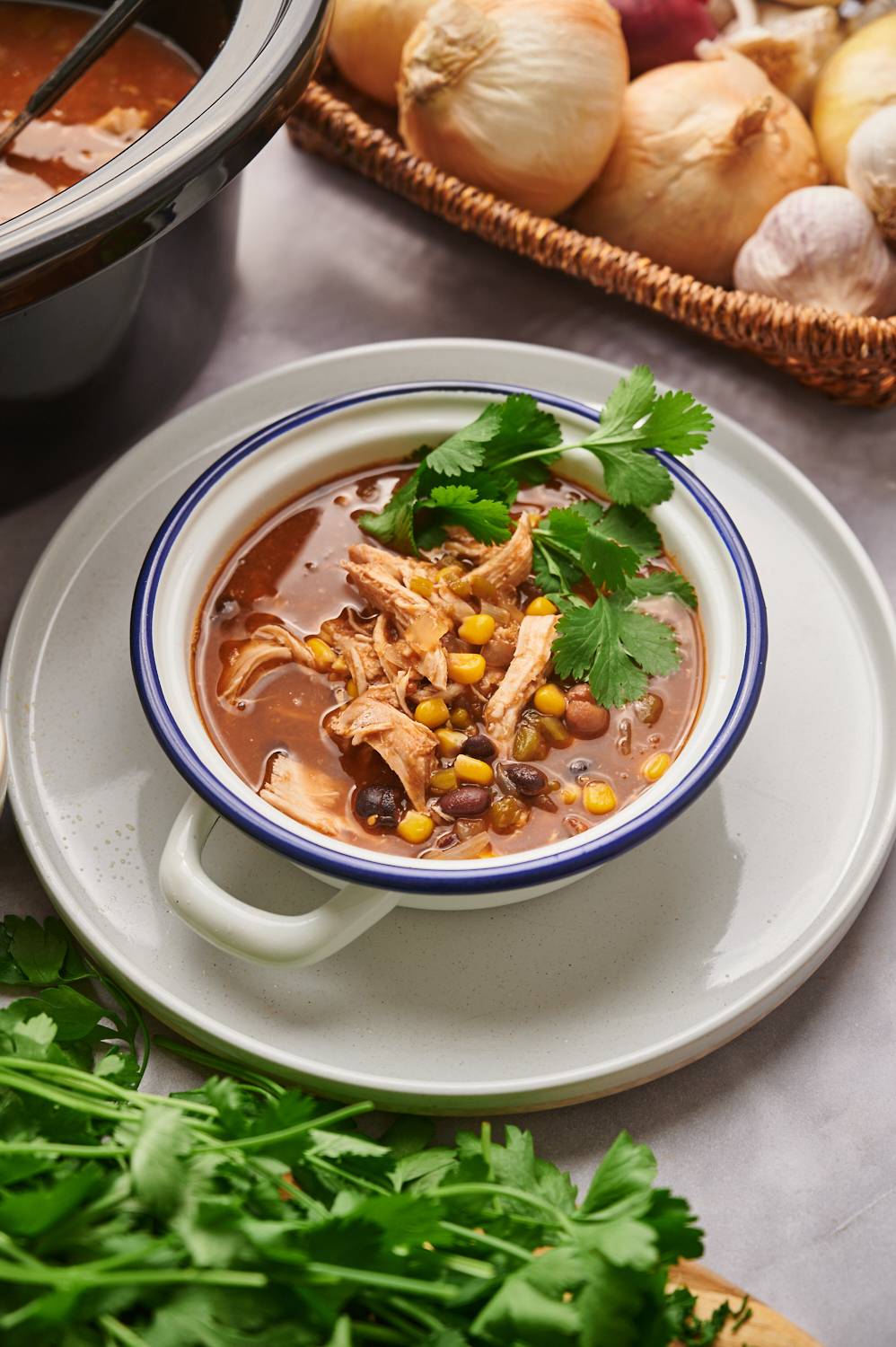 Chicken taco soup in a bowl with beans, chicken, corn, avocado, cheese, and cilantro.