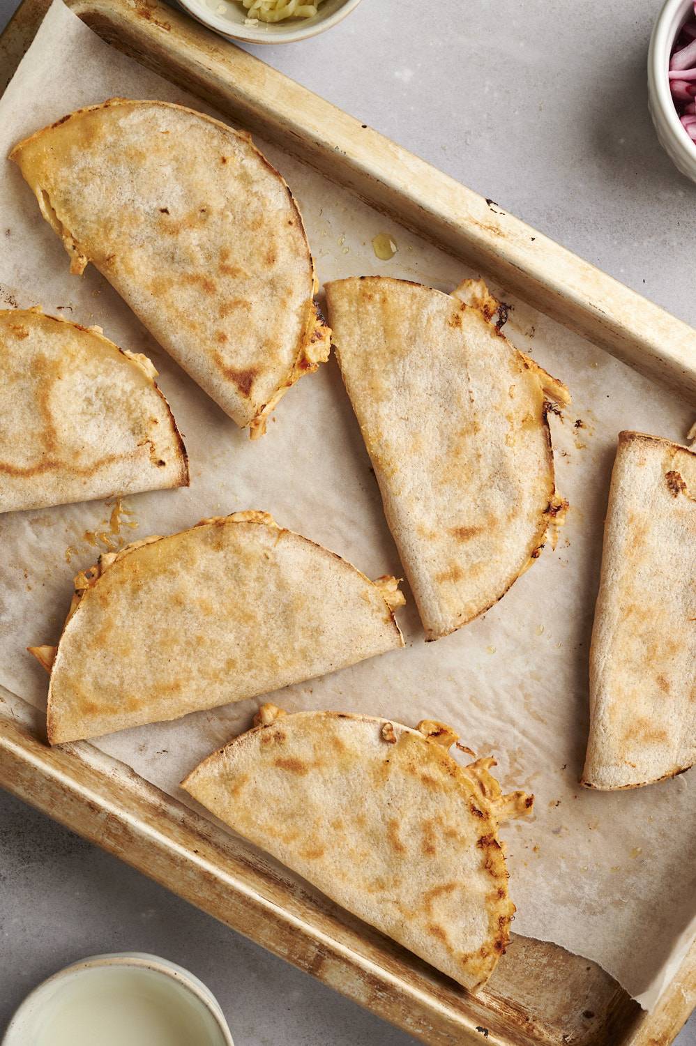 Crispy tacos dorados filled with creamy chicken on a baking sheet.