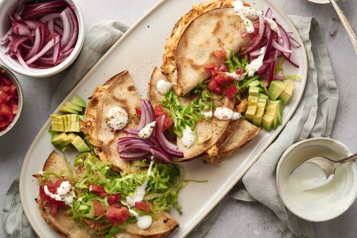 Tacos dorados filled with shredded chicken and served with avocado, onions, lettuce, salsa, and sour cream.