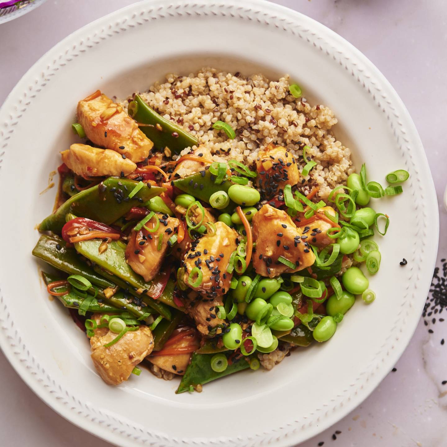 Teriyaki chicken bowls with chicken breast, snow peas, carrots, red pepper, and quinoa in a bowl with teriyaki sauce.