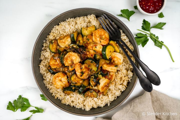 Thia baisl shrimp stir fry with zucchini, cooked shrimp, and brown rice in a bowl. 