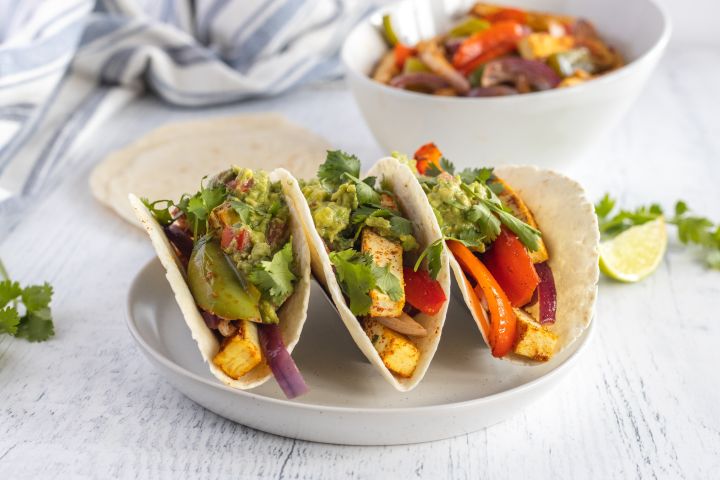 Tofu fajitas with extra firm tofu, red bell peppers, green bell peppers, and red onions cooked in spices served in flour tortillas with guacamole.