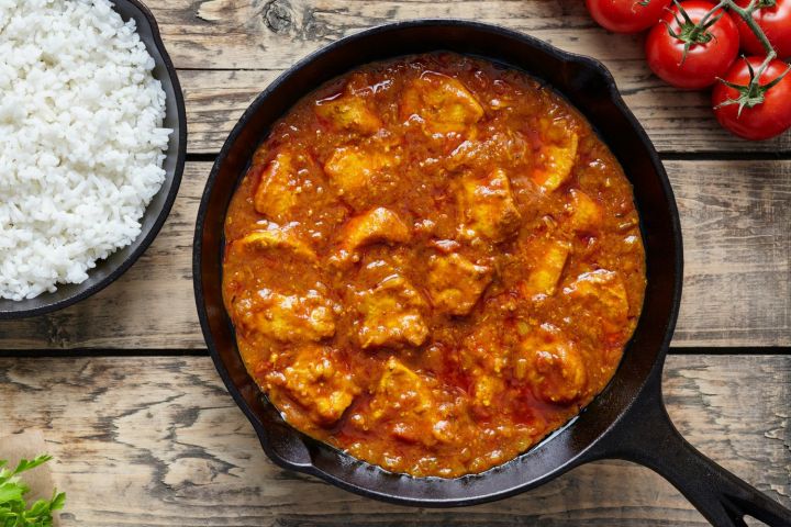 Tomato braised chicken thighs in a skillet with rice and tomatoes.