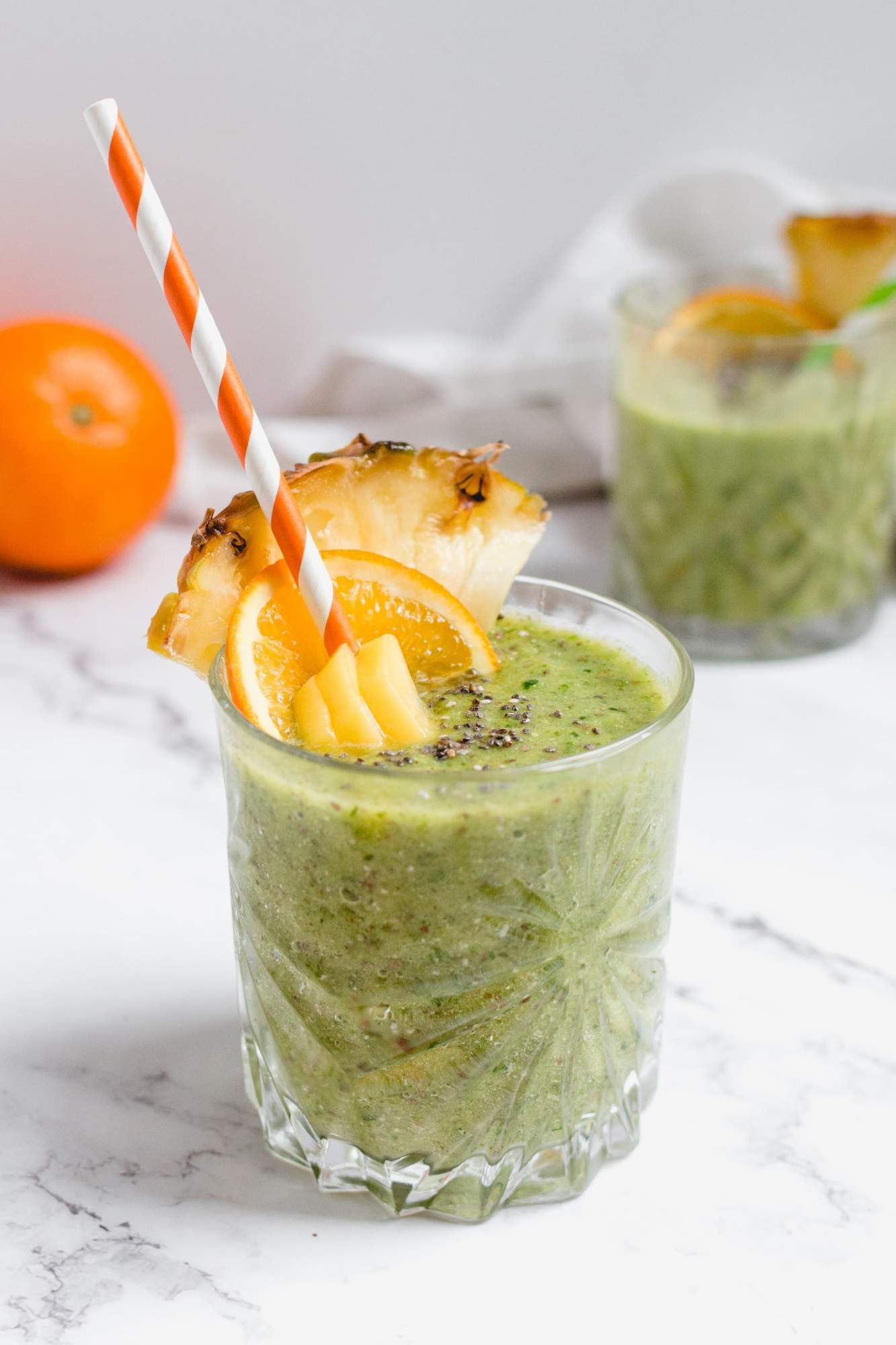 Pineapple kale smoothie with chia seeds and mango in a glass with a straw.