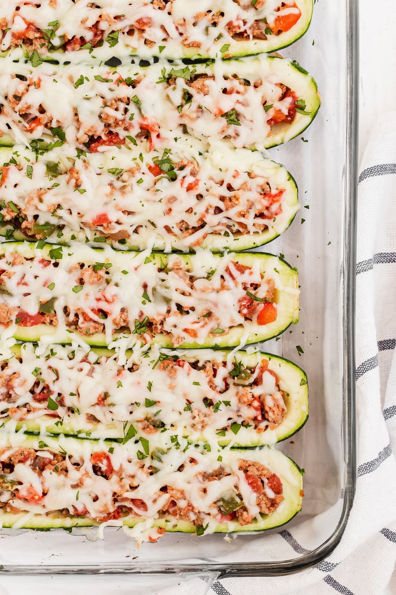 Zucchini boats with ground turkey, tomatoes, fajita seasoning, and melted cheese in a glass baking dish.