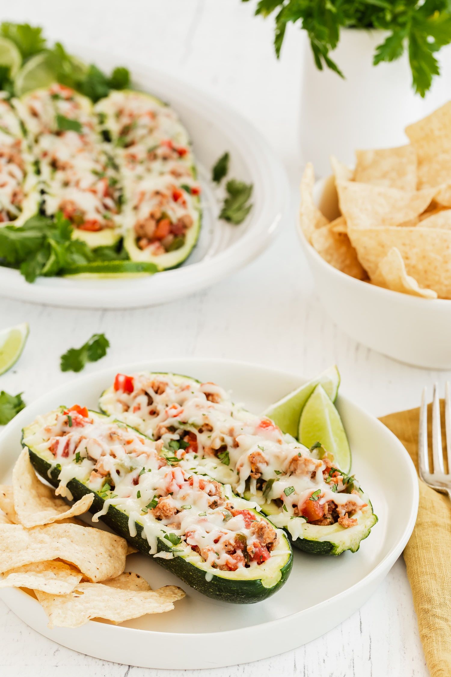 Zucchini boats with turkey fajita filling including tomatoes and melted cheese served with tortilla chips.