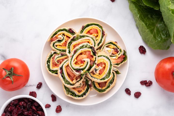 Turkey pinwheels with cream cheese, dried cranberries, cheddar cheese, lettuce, and tomatoes wrapped in a tortilla and sliced into pinwheels.