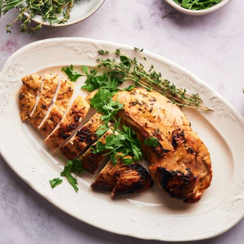 Baked turkey tenderloin sliced on a plate with fresh herbs.