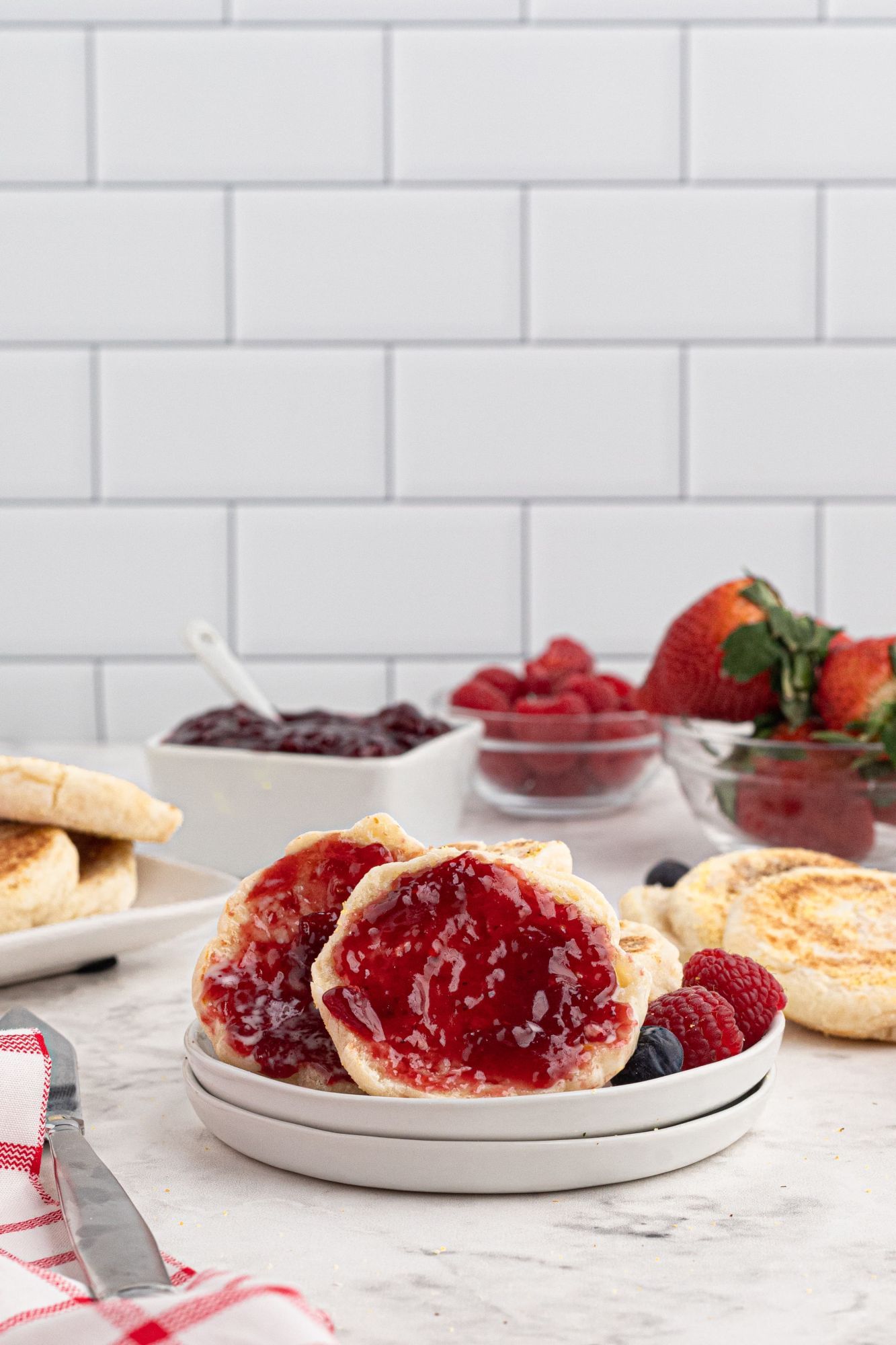 Homemade English muffins cut in half with served with strawberry jelly on a plate.