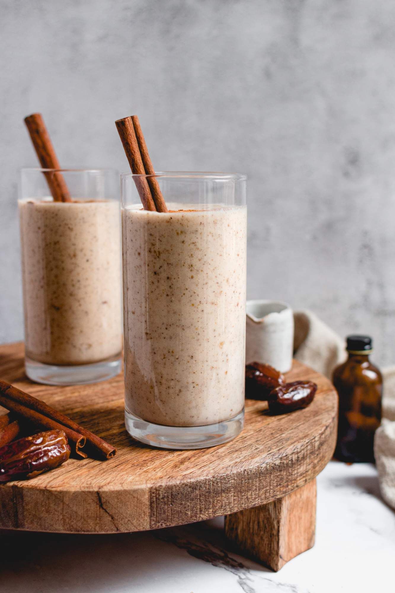 Vanilla protein shake with cinnamon and almond butter in two glasses with cinnamon sticks and dates.