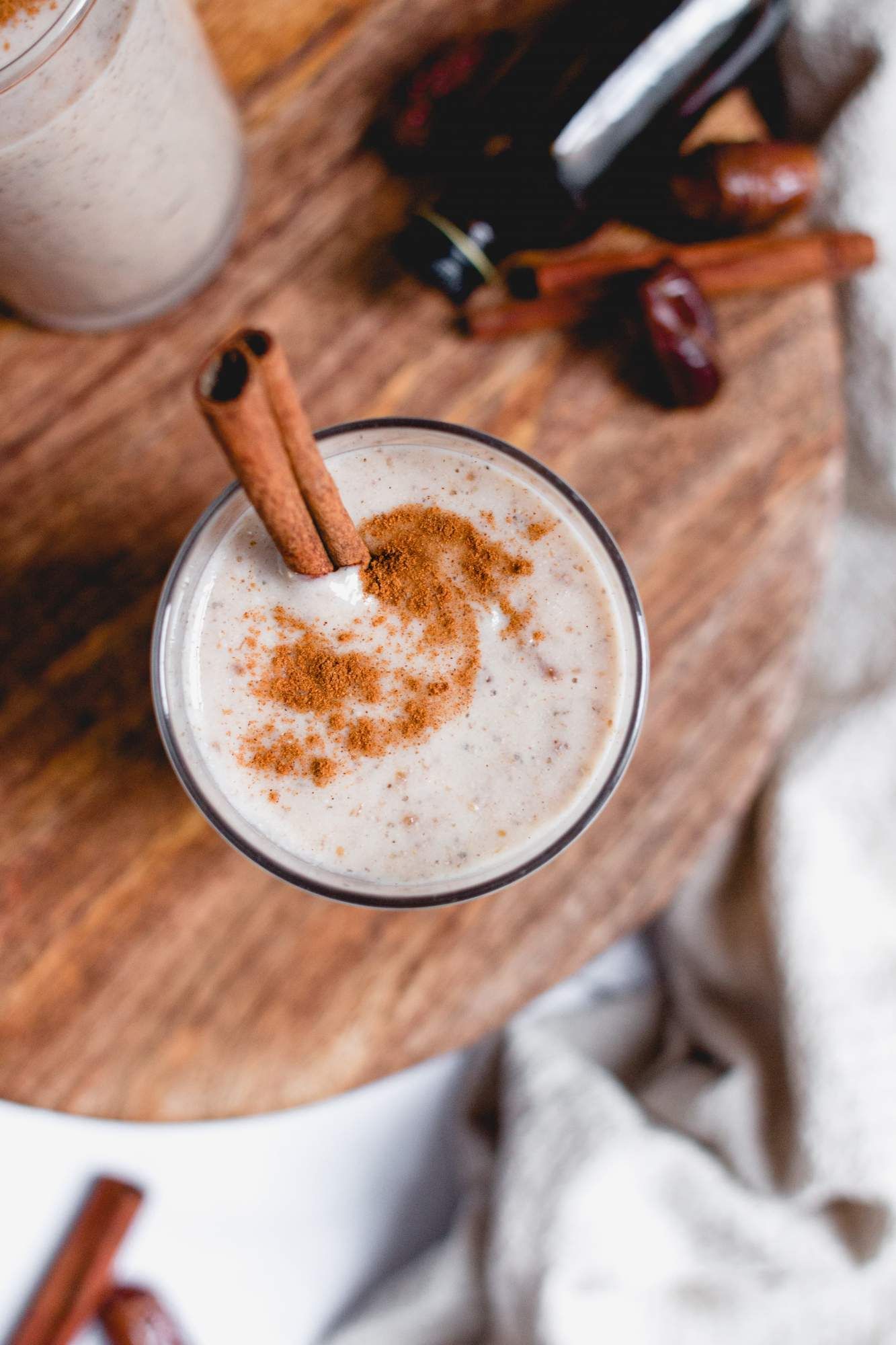 Protein shake with bananas, cinnamon, almond butter, and dates in a glass on a wooden cutting board.