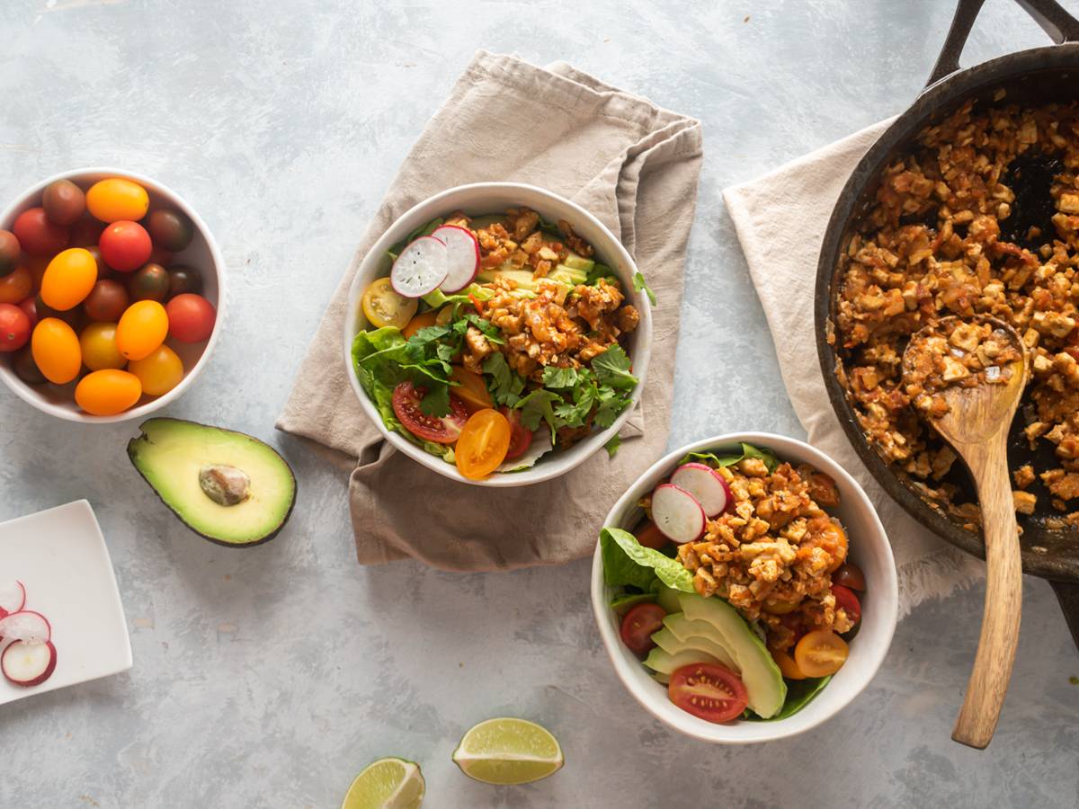 Chipotle Sofritas tofu in a skillet and served in bowls with lettuce, avocado, tomato, and cilantro.