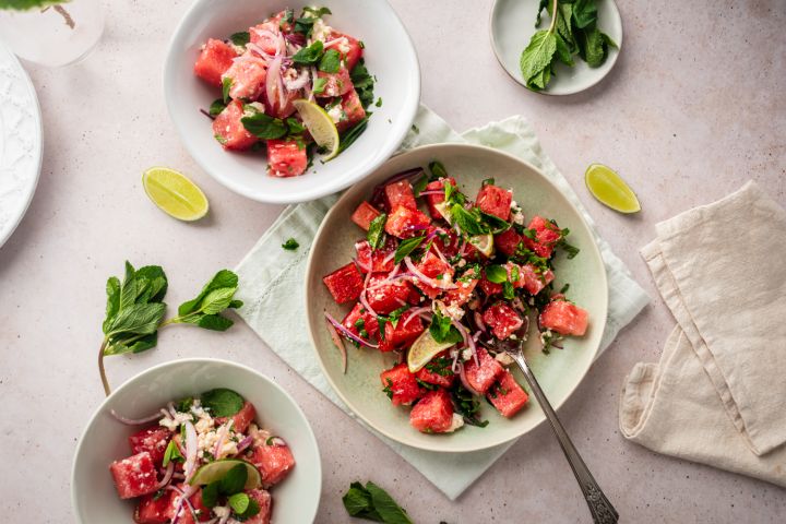 Watermelon, feta, and mint salad served in three bowls with sliced red onion, crumbled feta, cubed watermelon, and lime juice.