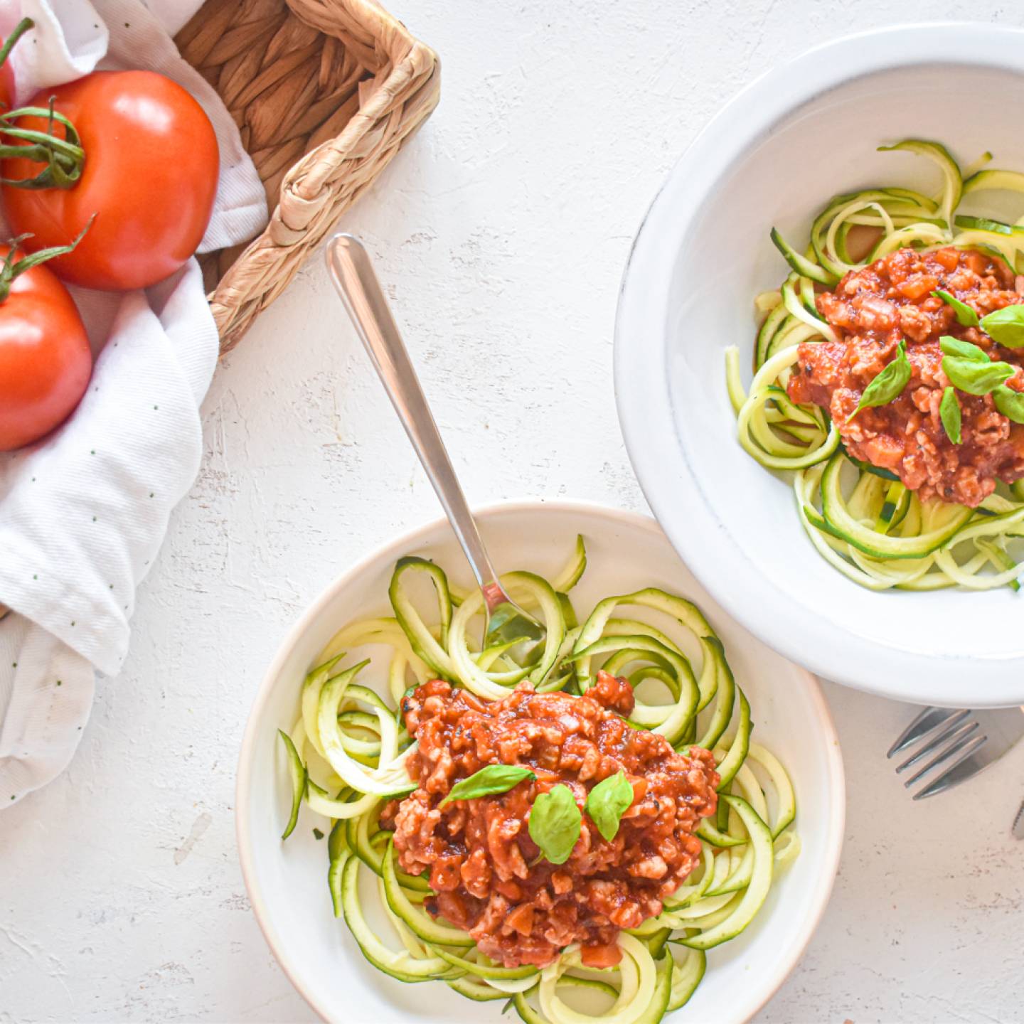 Zucchini noodle bolognese with zucchni noodles, turkey bolognese sauce, and basil on a plate with tomatoes on the side.