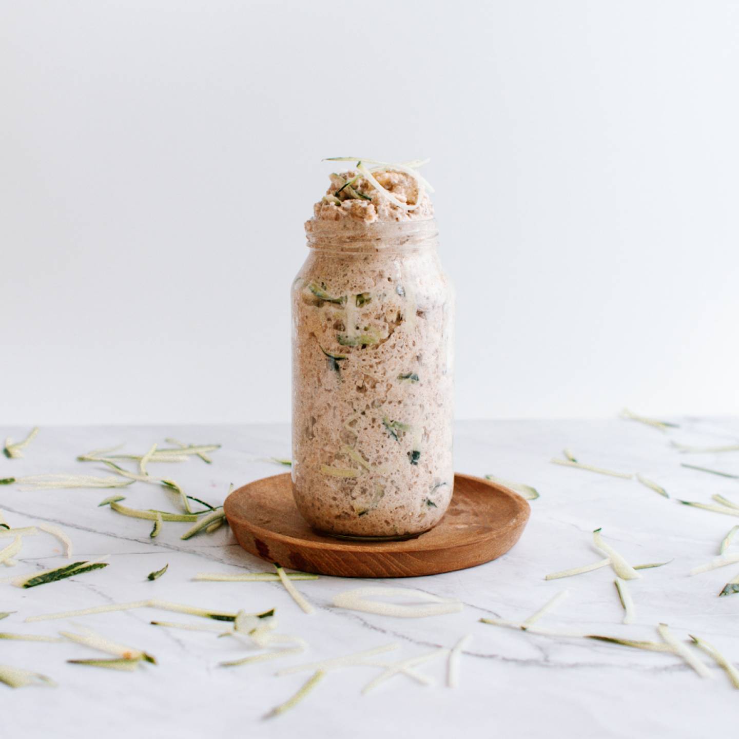 Zucchini bread overnight oatmeal in a glass jar with cinnamon, rolled oats, almond butter, and shredded zucchini.