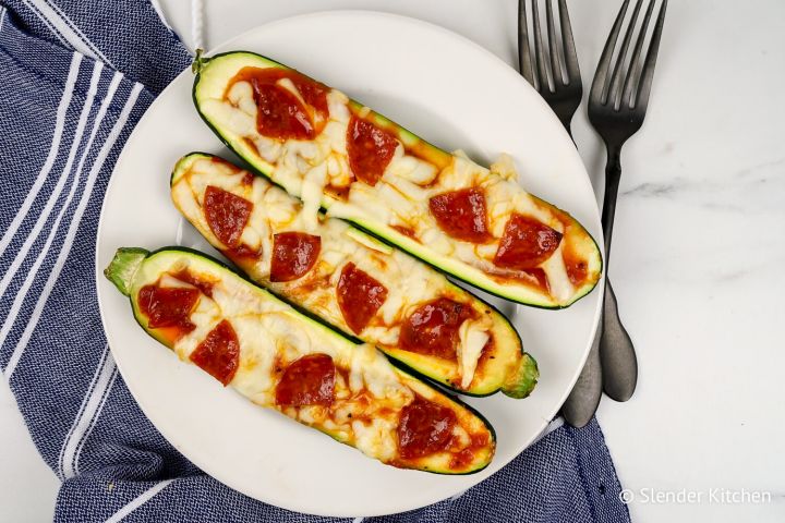 Zucchini pizza boats with marinara sauce, melted mozzarella cheese, and pepperoni on a white plate.